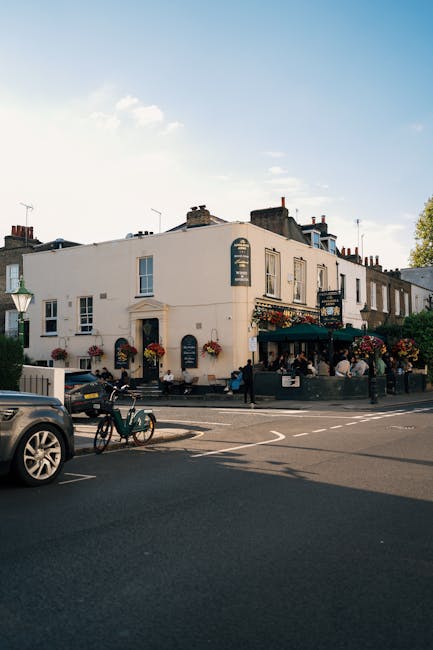 The image shows a street scene outside a traditional UK pub, located within a white-painted building with a slightly curved facade. The pub's exterior features decorative elements such as hanging flow